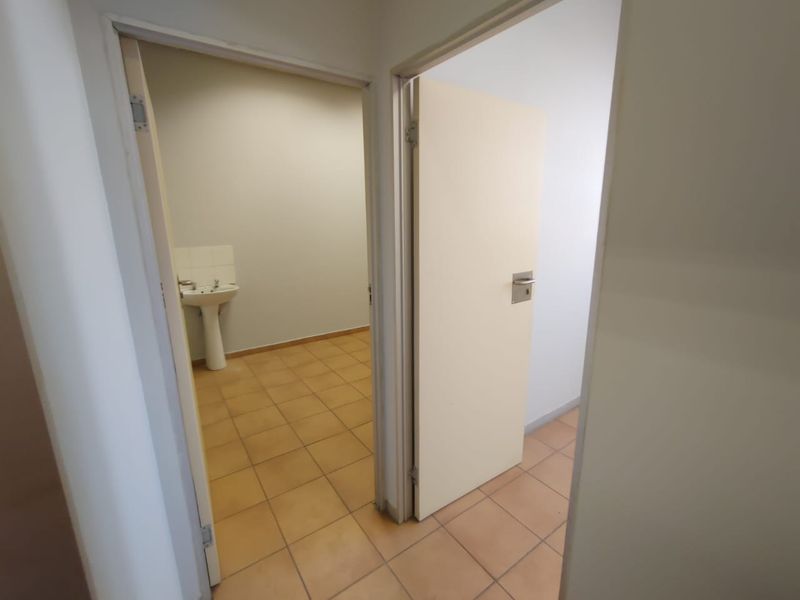 A functional hallway area featuring ceramic floor tiles and access to a small room equipped with a pedestal basin.