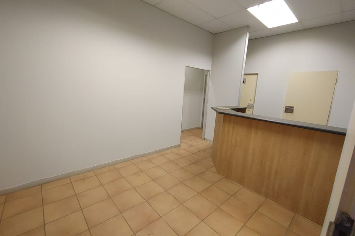 Empty commercial office space featuring a built-in reception counter, tiled flooring, and a drop ceiling with recessed lighting.