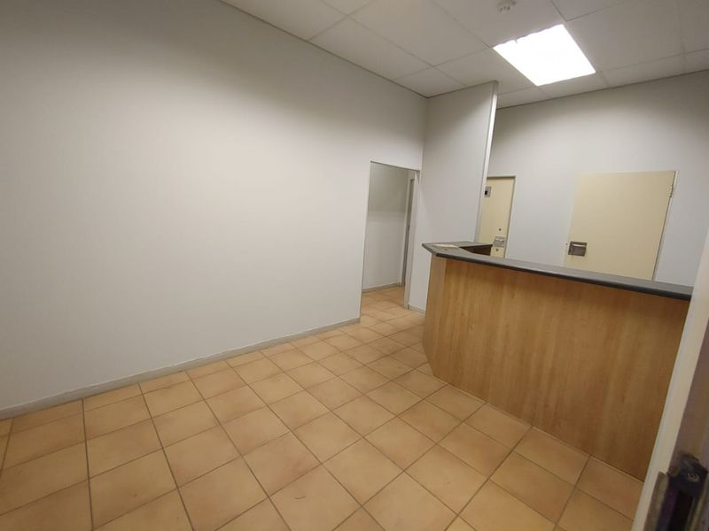 Empty commercial office space featuring a built-in reception counter, tiled flooring, and a drop ceiling with recessed lighting.