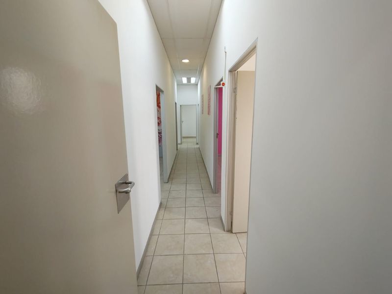 A functional commercial hallway featuring tiled flooring, recessed ceiling lights, and multiple internal access doors.