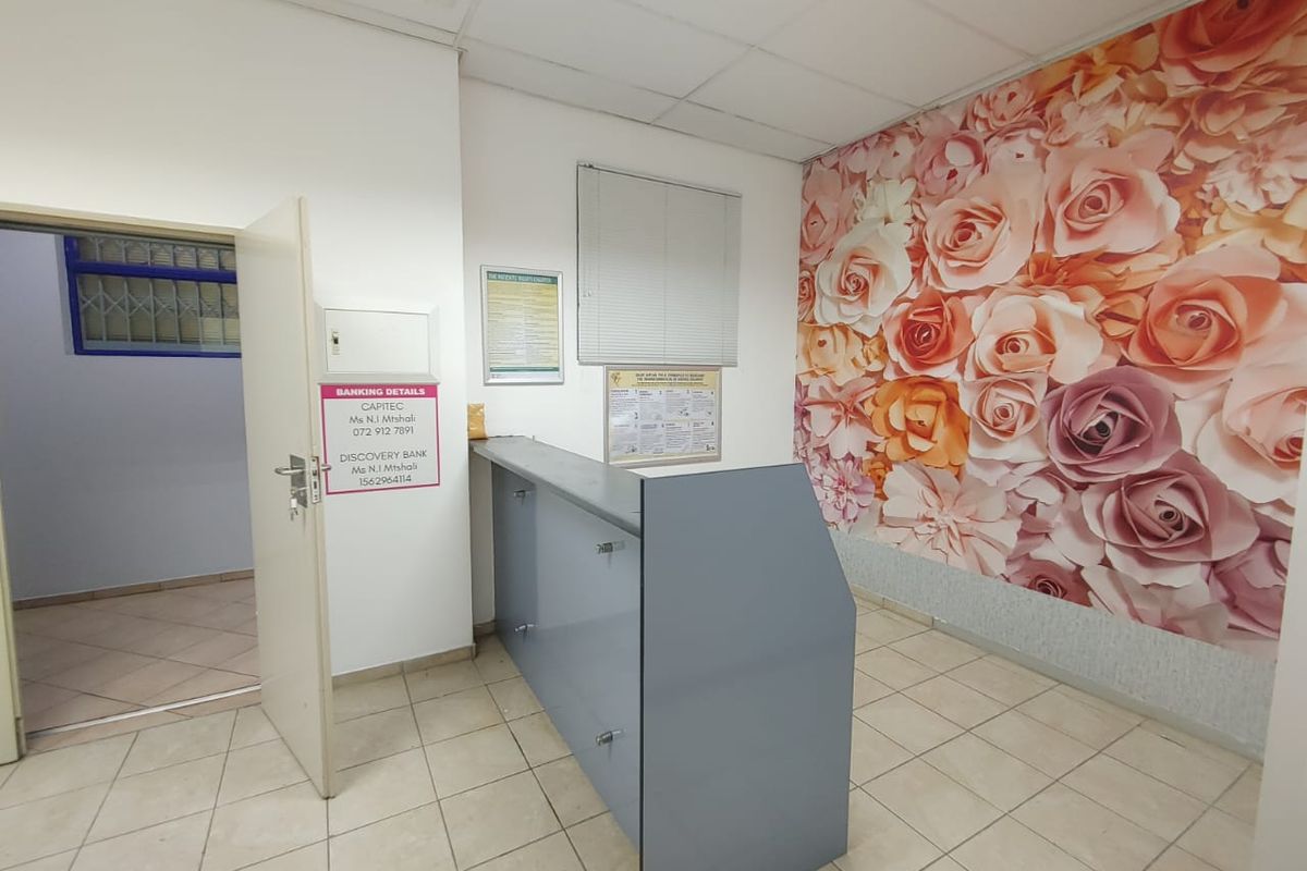 Commercial office space featuring a built-in reception desk, tiled flooring, drop ceiling, and a decorative floral feature wall.