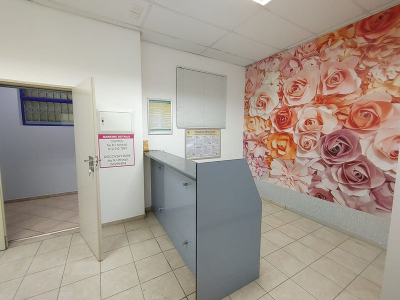 Commercial office space featuring a built-in reception desk, tiled flooring, drop ceiling, and a decorative floral feature wall.