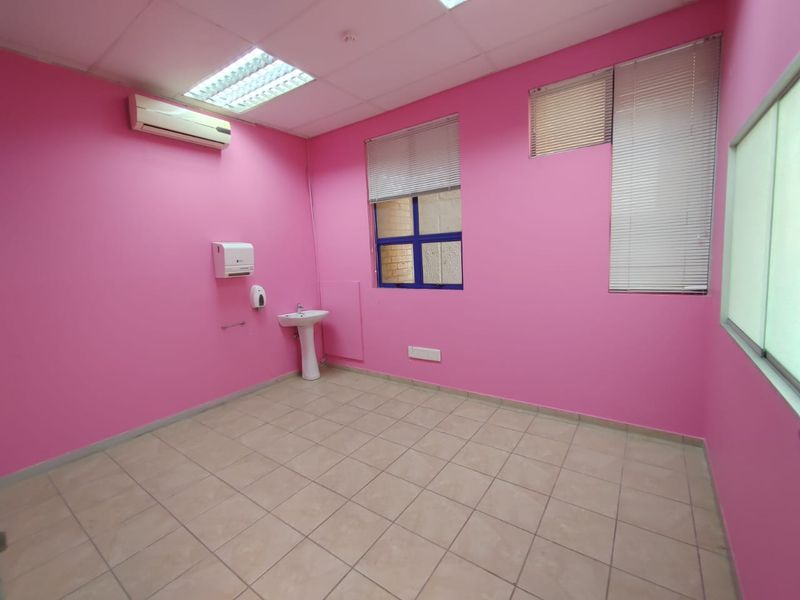 An empty office space featuring bright pink walls, tiled flooring, a pedestal washbasin, and wall-mounted air conditioning.