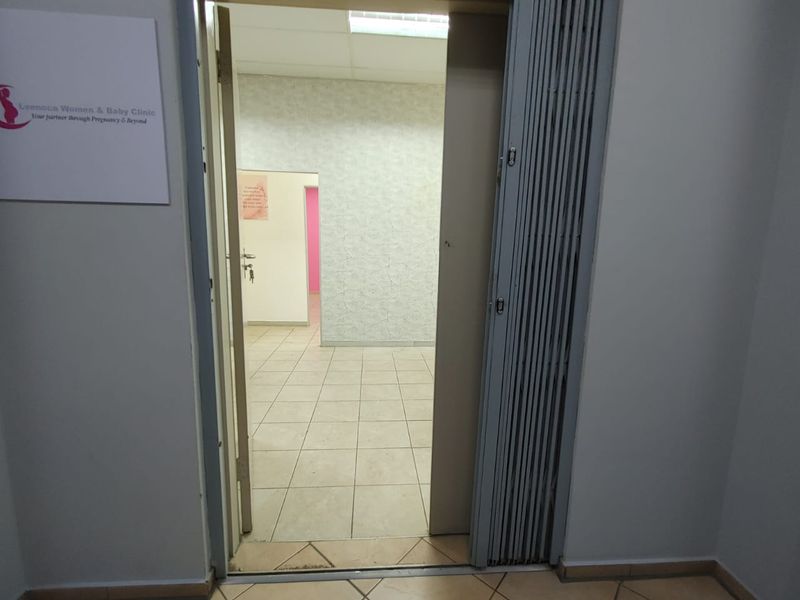 An empty commercial hallway featuring tiled flooring, a retractable accordion door, and a drop ceiling with integrated lighting.
