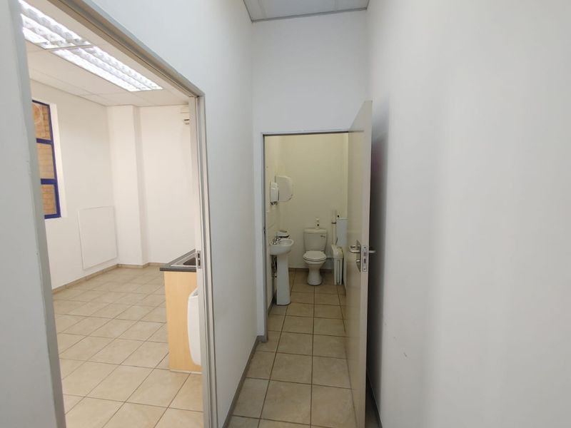 A functional commercial hallway providing access to a small kitchenette area and a private restroom with standard fixtures.