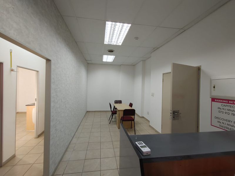 A functional commercial office space featuring tiled flooring, a built-in reception counter, and recessed ceiling lighting, suitable for professional use.