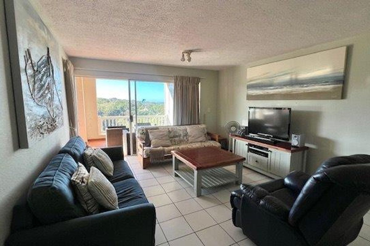 A comfortable living room featuring tiled flooring and a large sliding glass door that provides access to an outdoor balcony area.