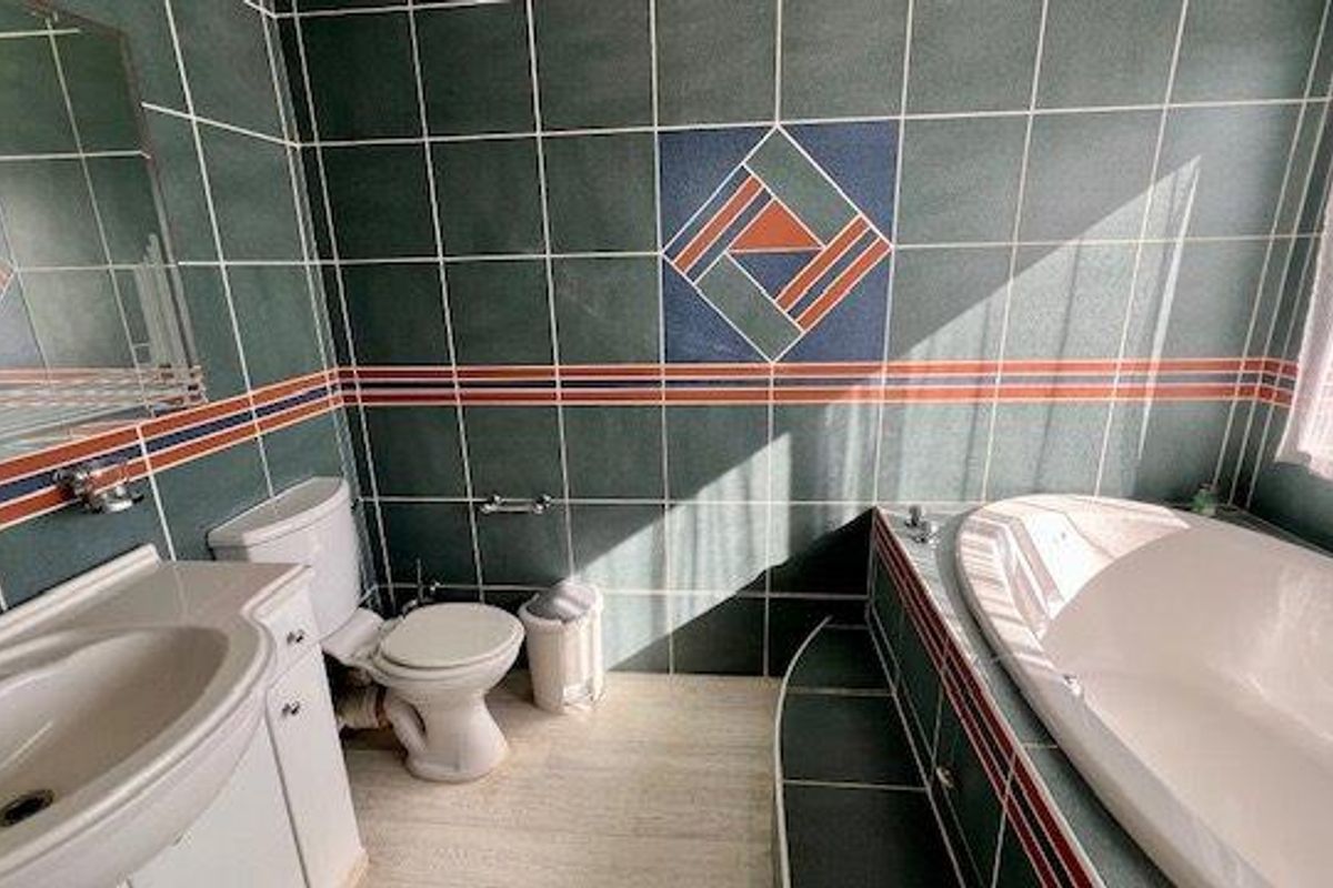 A dated bathroom featuring decorative green wall tiles, a built-in bathtub, and a vanity unit with a basin.