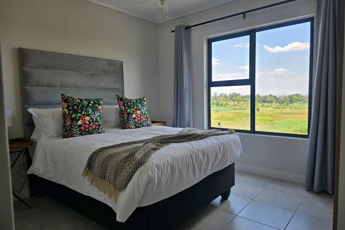 A bright and modern bedroom featuring tiled flooring, a large aluminium window with scenic views, and neutral wall finishes.