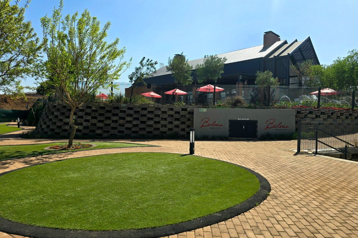 A well-maintained exterior area featuring a paved courtyard, circular artificial lawn, and a modern building with a metal roof and retaining wall structure.