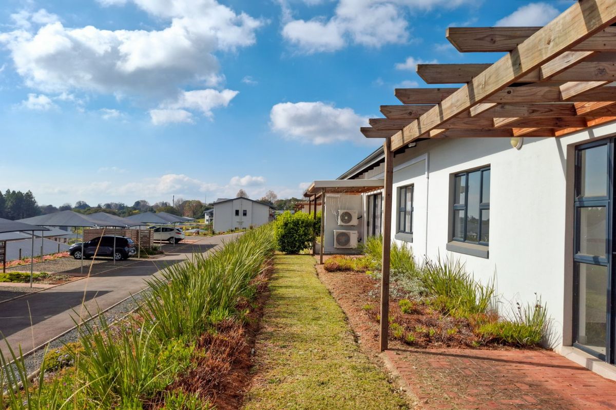 Rear exterior view of the townhouse featuring a timber pergola, brick paved patio, and landscaped garden beds with adjacent parking area.