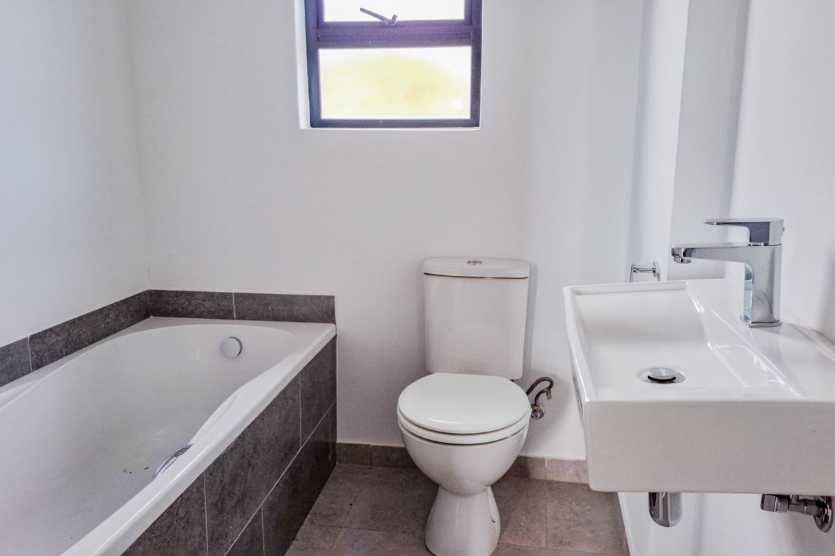 A clean, functional bathroom featuring a built-in bathtub with tiled surround, a wall-mounted basin, and a standard toilet.