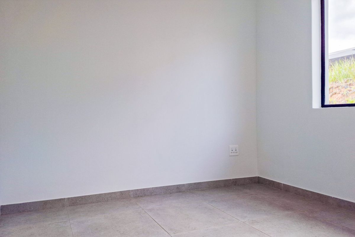 A clean, empty bedroom featuring neutral tiled flooring, white walls, and a window providing natural light.