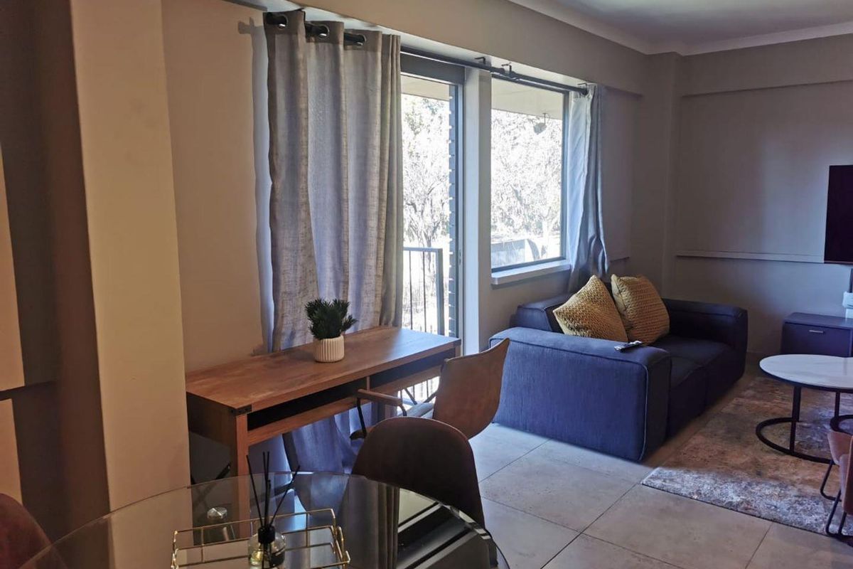 A well-lit living area featuring neutral tiled flooring and a sliding glass door providing access to an outdoor balcony space.