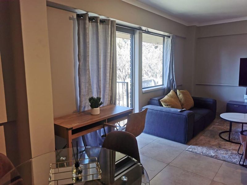 A well-lit living area featuring neutral tiled flooring and a sliding glass door providing access to an outdoor balcony space.