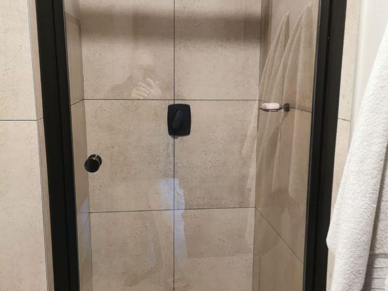 A modern walk-in shower featuring neutral wall tiles, a black-framed glass door, and a contemporary rainfall shower head.