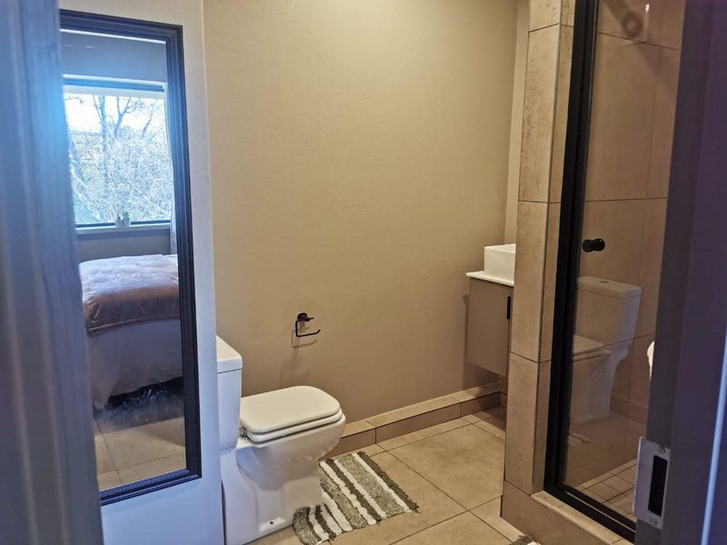 A modern bathroom featuring a tiled shower enclosure, a wall-mounted vanity with a vessel sink, and a standard toilet.