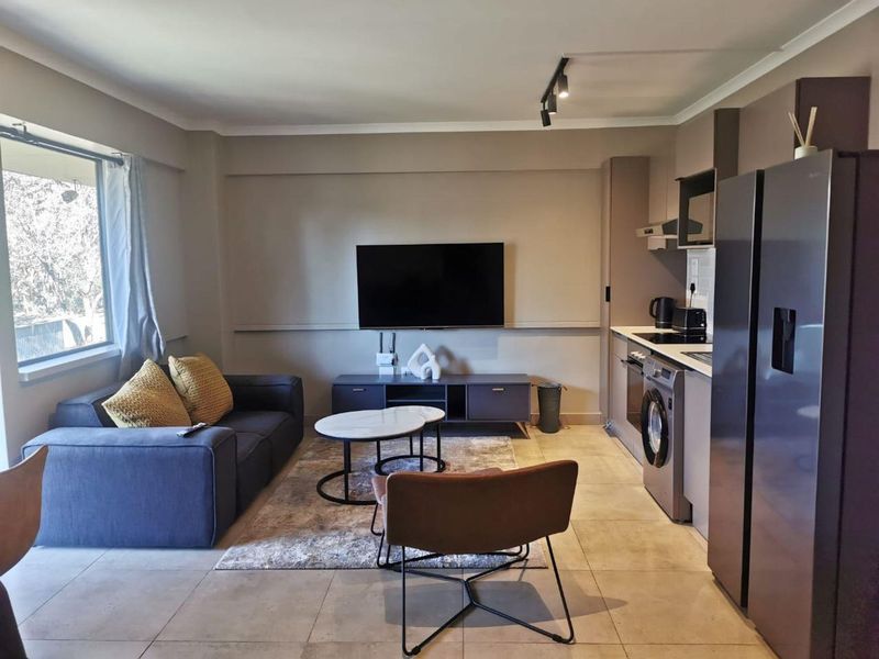 Modern open-plan living area featuring a compact kitchen with built-in appliances, tiled flooring, and track lighting, creating a functional and cohesive living space.