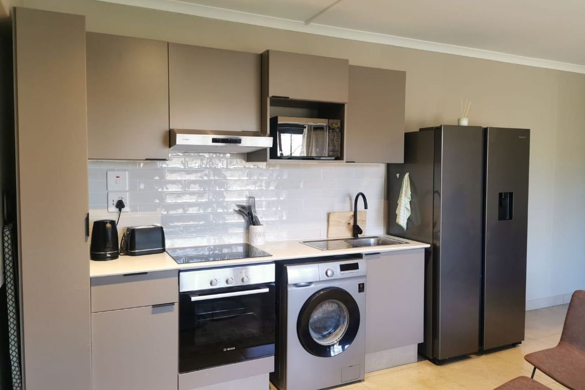 Modern kitchen featuring sleek taupe cabinetry, subway tile backsplash, integrated appliances including an oven, hob, and extractor fan, with a clean, functional layout.