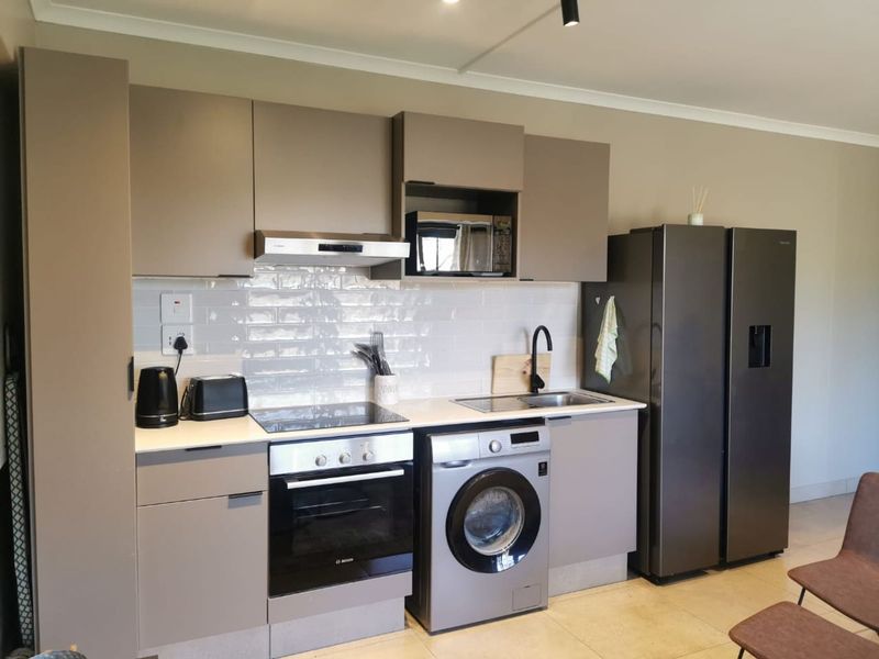 Modern kitchen featuring sleek taupe cabinetry, subway tile backsplash, integrated appliances including an oven, hob, and extractor fan, with a clean, functional layout.