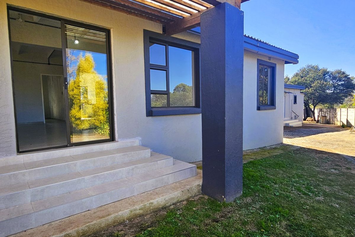 Rear exterior view of the house featuring a tiled entrance with sliding glass doors, a timber pergola, and a paved driveway area.