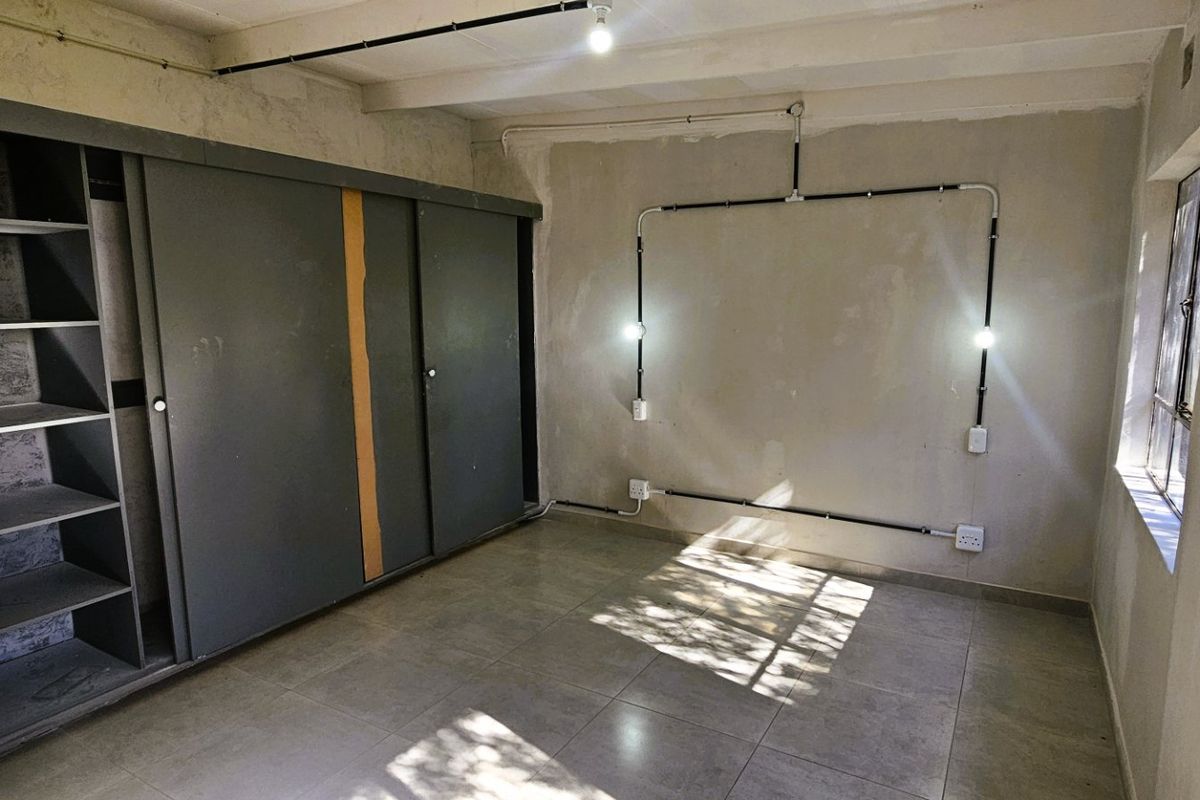 A bedroom featuring tiled flooring, built-in sliding wardrobe, and exposed electrical conduit, requiring cosmetic updates to improve the overall finish and aesthetic.