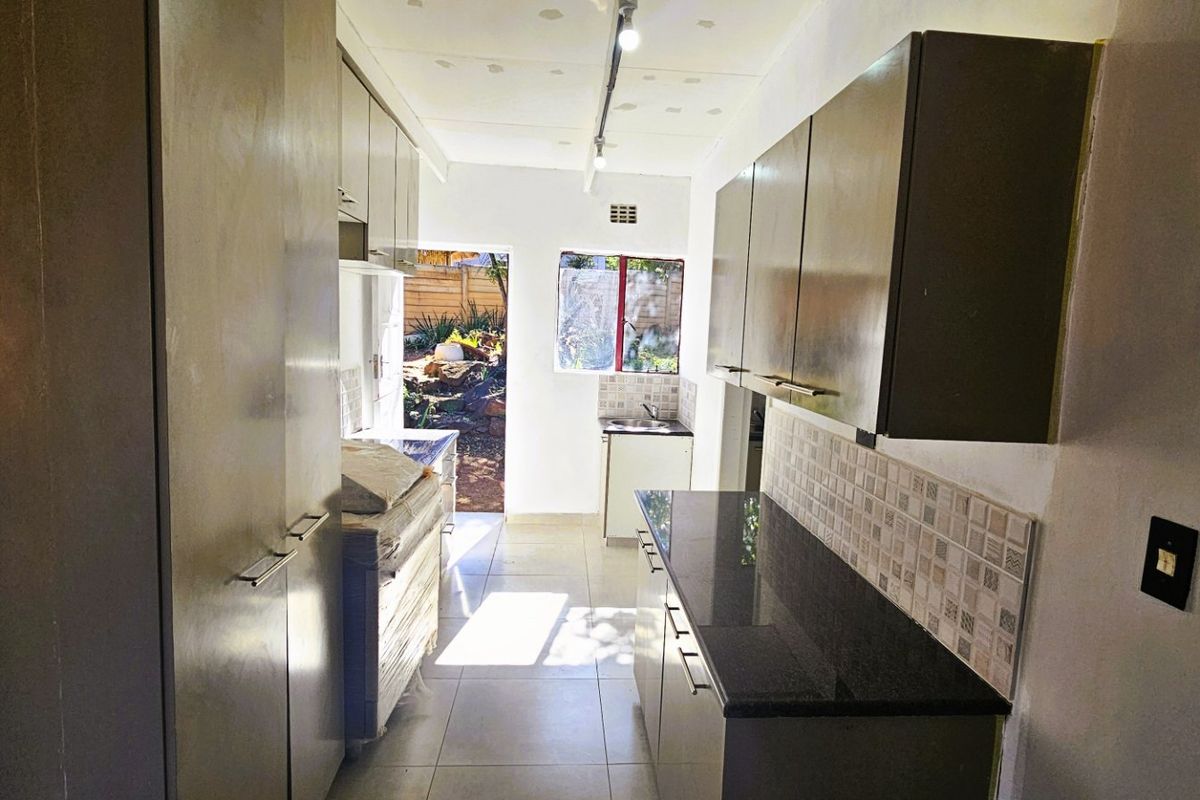 A galley-style kitchen featuring dark cabinetry, granite countertops, tiled backsplash, and direct access to the rear garden area.