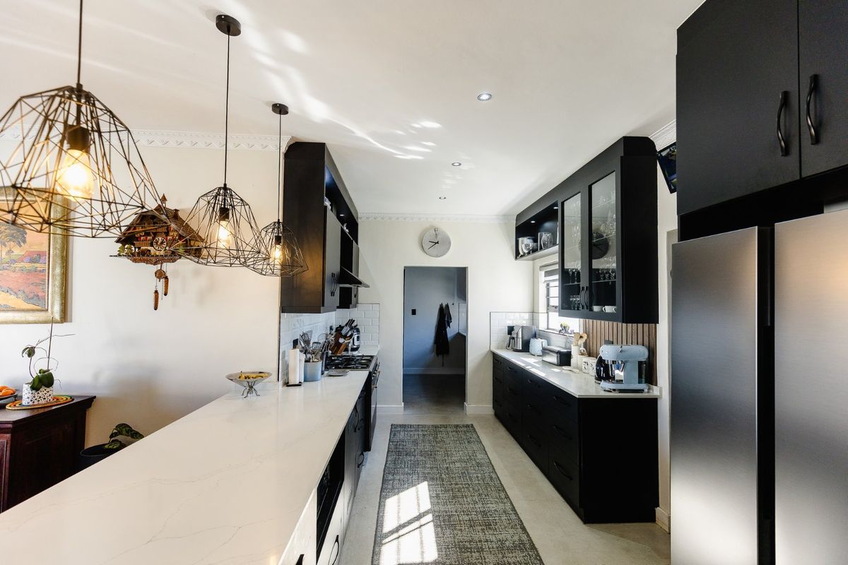 Modern kitchen featuring sleek black cabinetry, white quartz countertops, subway tile backsplash, and stylish pendant lighting, creating a sophisticated and functional culinary space.