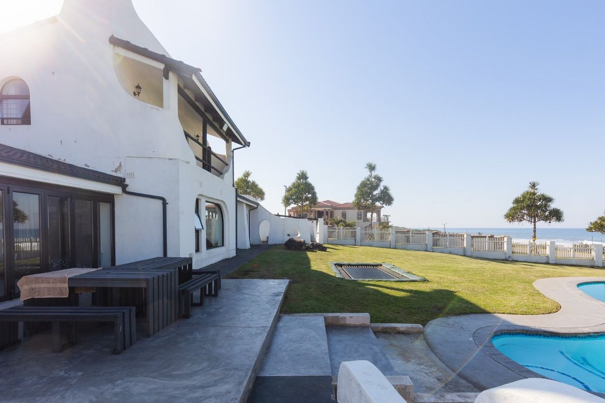 Rear exterior view featuring a swimming pool, concrete patio area, and a landscaped garden with ocean views.