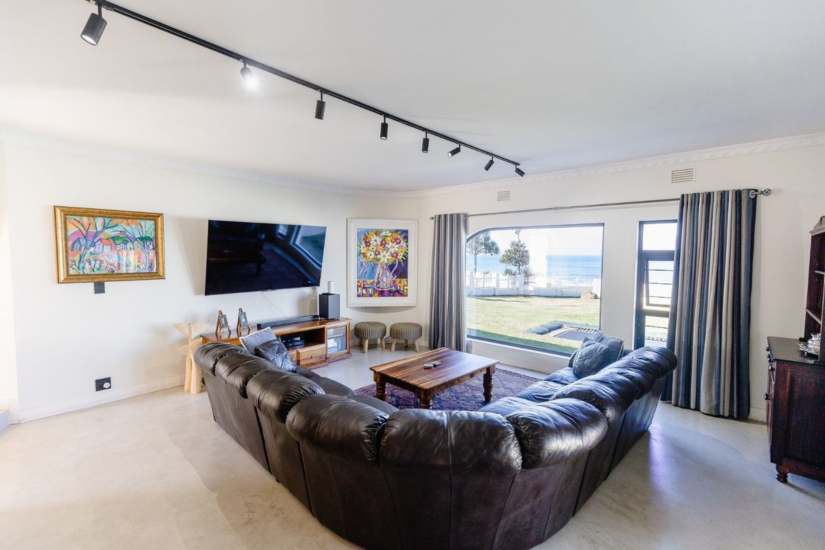 Spacious living room featuring modern track lighting, tiled floors, and a large picture window offering scenic views of the garden and ocean.
