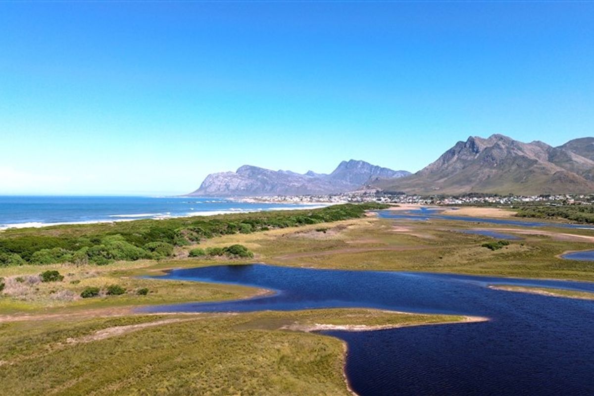 An aerial view of the coastal landscape featuring wetlands, natural vegetation, and a scenic mountain range in the background.