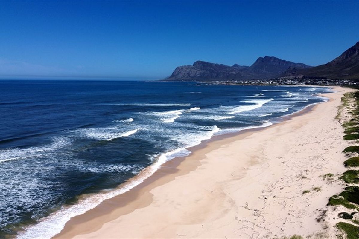 An aerial view of the pristine coastline, showcasing the sandy beach, ocean waves, and distant mountain range.