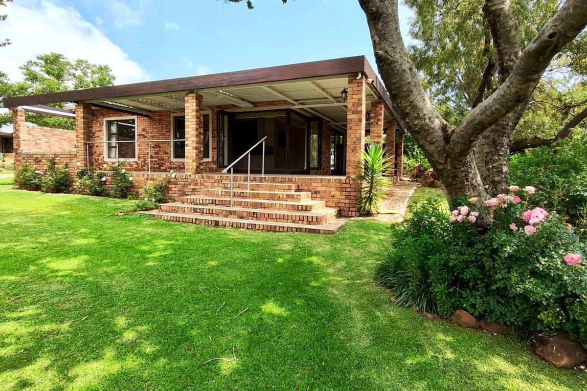 A well-maintained face brick house featuring a spacious covered patio with folding glass doors, overlooking a lush, landscaped garden.