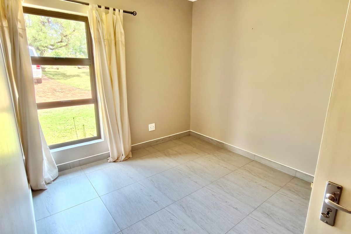 A bright, empty bedroom featuring neutral wall tones, tiled flooring, and a large window providing natural light and garden views.