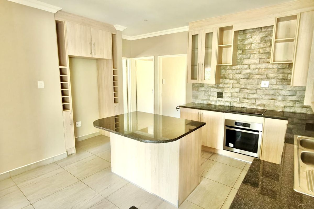 Modern kitchen featuring light wood cabinetry, stone countertops, a central island, built-in oven, and a decorative stone tile backsplash.