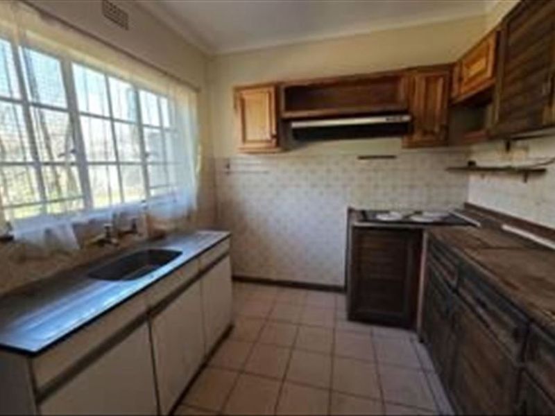 A dated kitchen featuring wooden cabinetry, tiled flooring, and a stainless steel sink, offering significant potential for modernization and renovation.