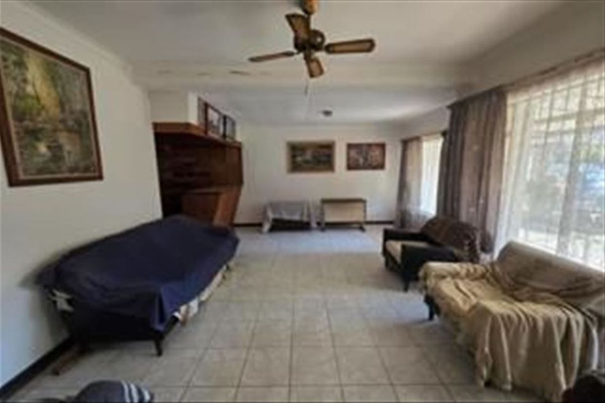Spacious living room featuring tiled flooring, a ceiling fan, and a built-in bar area, offering a functional layout with potential for modernization.