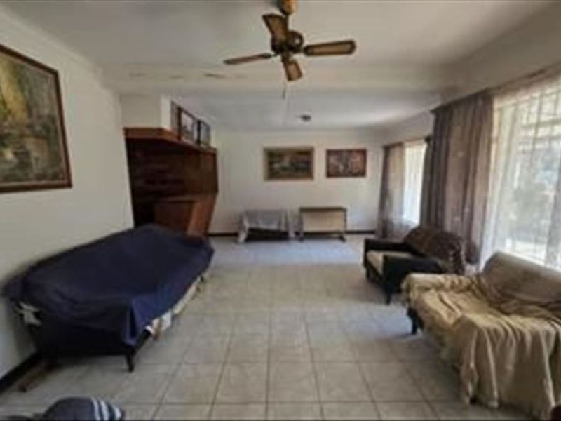 Spacious living room featuring tiled flooring, a ceiling fan, and a built-in bar area, offering a functional layout with potential for modernization.