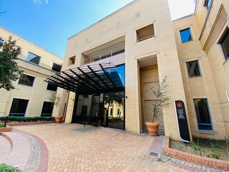 The front entrance of a commercial office building featuring a brick facade, a modern glass canopy, and a paved entrance area.