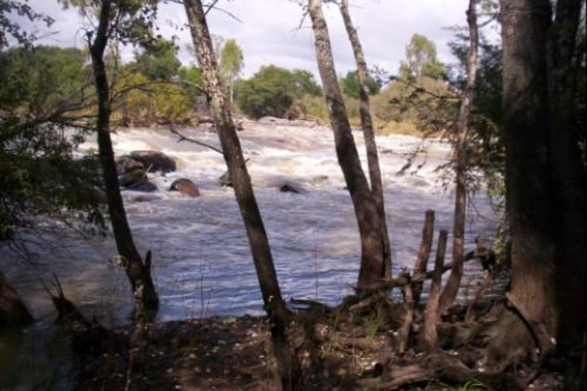 A scenic view of a flowing river with natural rocky features and surrounding mature trees, highlighting the property's natural landscape.