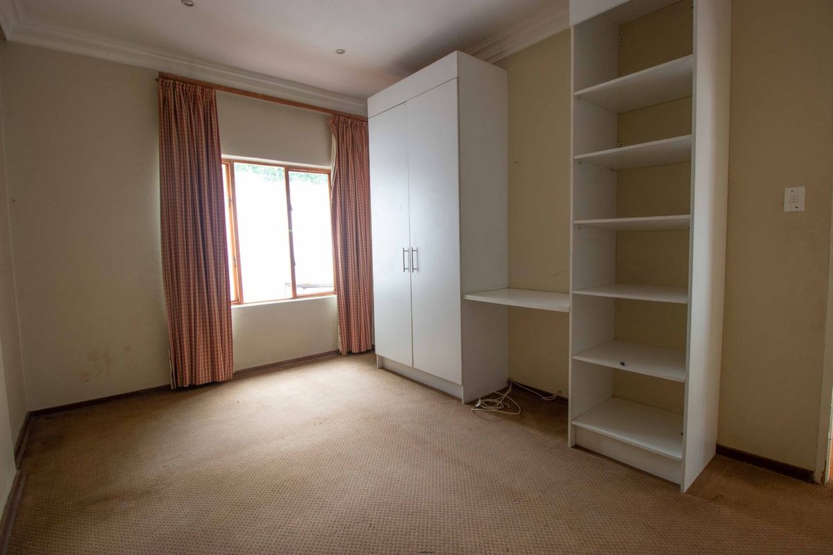 A vacant bedroom featuring built-in white cabinetry, shelving, and carpeted flooring, offering a blank canvas for potential updates and interior design.