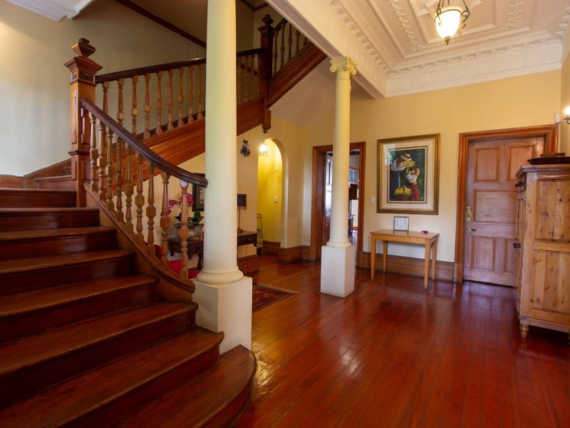 Grand entrance hall featuring polished hardwood flooring, a sweeping wooden staircase, classical columns, and intricate ceiling detailing, showcasing traditional architectural character.