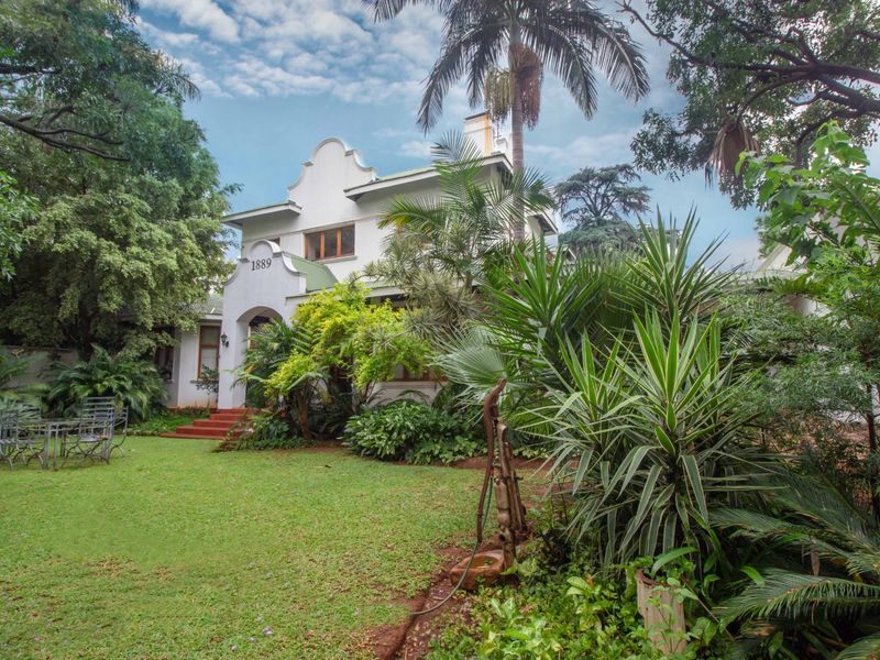 A charming Cape Dutch style house featuring a distinctive gable, well-maintained garden, and mature trees, showcasing classic architectural character.