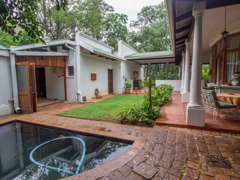 Outdoor entertainment area featuring a swimming pool, brick-paved patio, and a covered veranda supported by classical columns.