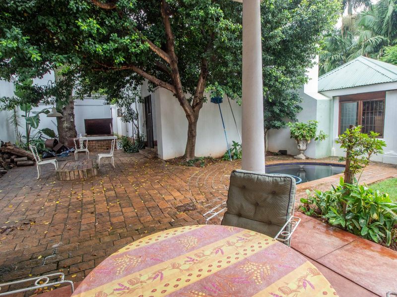 Outdoor patio area featuring brick paving, a built-in braai, and a small plunge pool, shaded by mature trees.