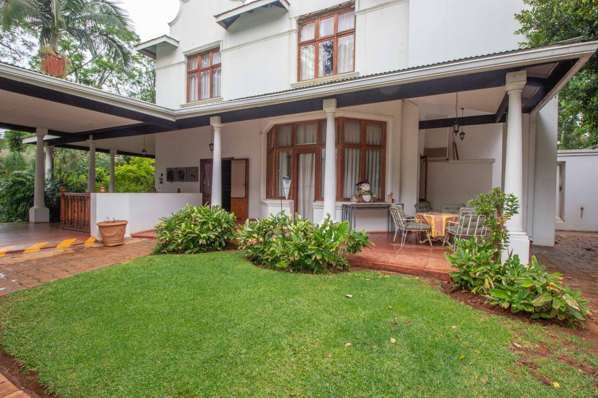A spacious rear exterior view featuring a covered patio with tiled flooring, classic support columns, and a well-maintained garden lawn.