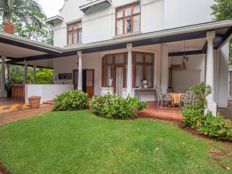 A spacious rear exterior view featuring a covered patio with tiled flooring, classic support columns, and a well-maintained garden lawn.
