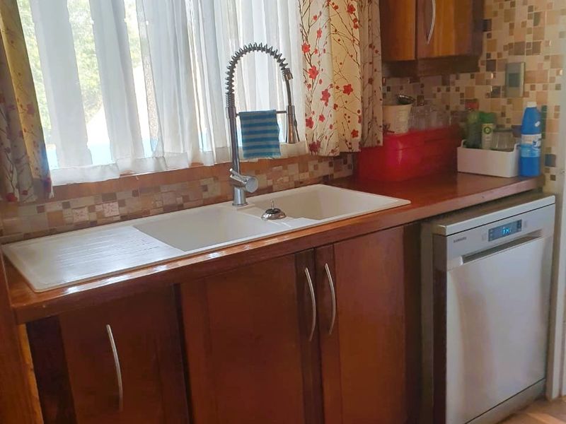 Kitchen area featuring wooden cabinetry, a double basin sink with gooseneck faucet, mosaic tile backsplash, and an integrated dishwasher.