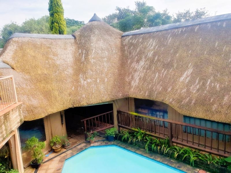 An elevated view of a swimming pool area featuring a traditional thatch roof structure and timber balcony railings.