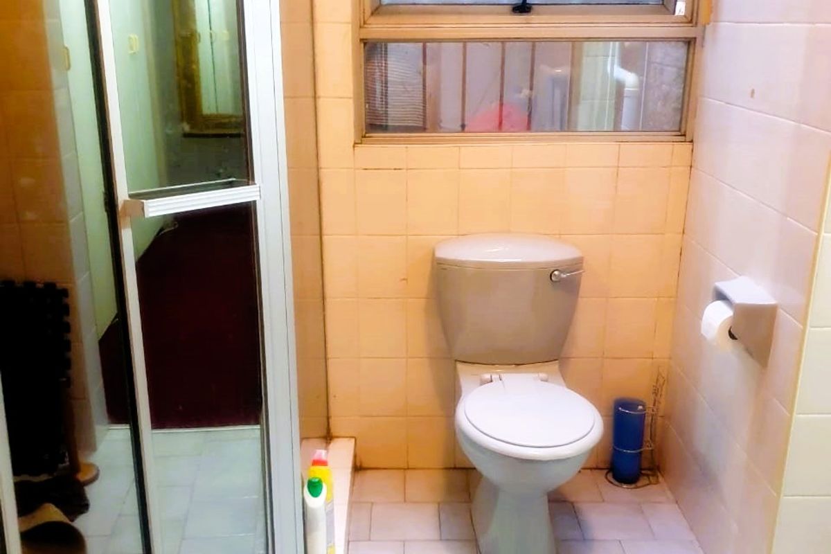 A compact bathroom featuring a shower enclosure, toilet, and tiled finishes, requiring cosmetic updates to modernize the space.